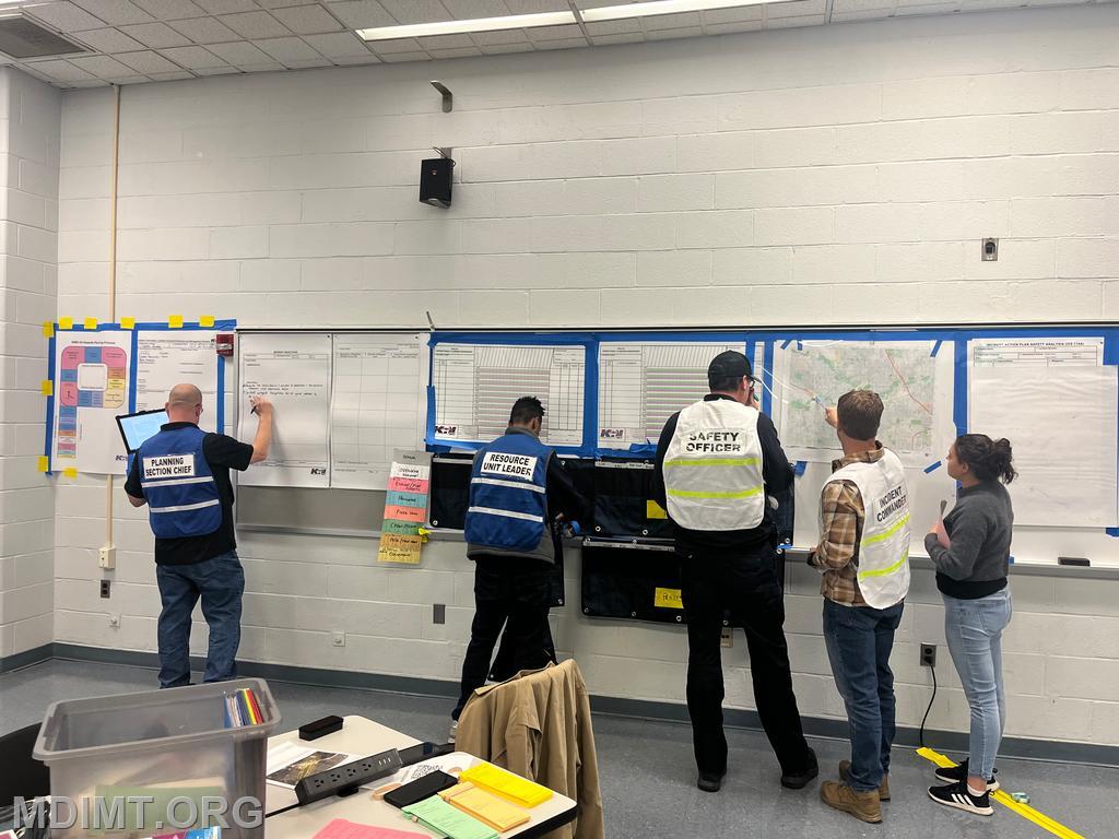 Red Team IC Jonathan Zimmer discusses current ops with DOSC Taylor Munir and SOFR Jason Hardesty. RESL Evan Mason works the &quot;T&quot; Card rack as PSC Michael Lambert post the objectives.